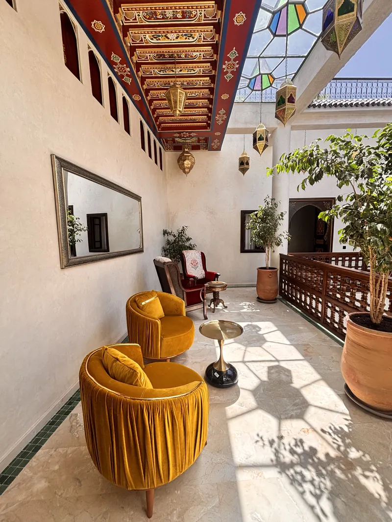 The gallery salon: ochre armchairs, mirror and plants under the painted ceiling