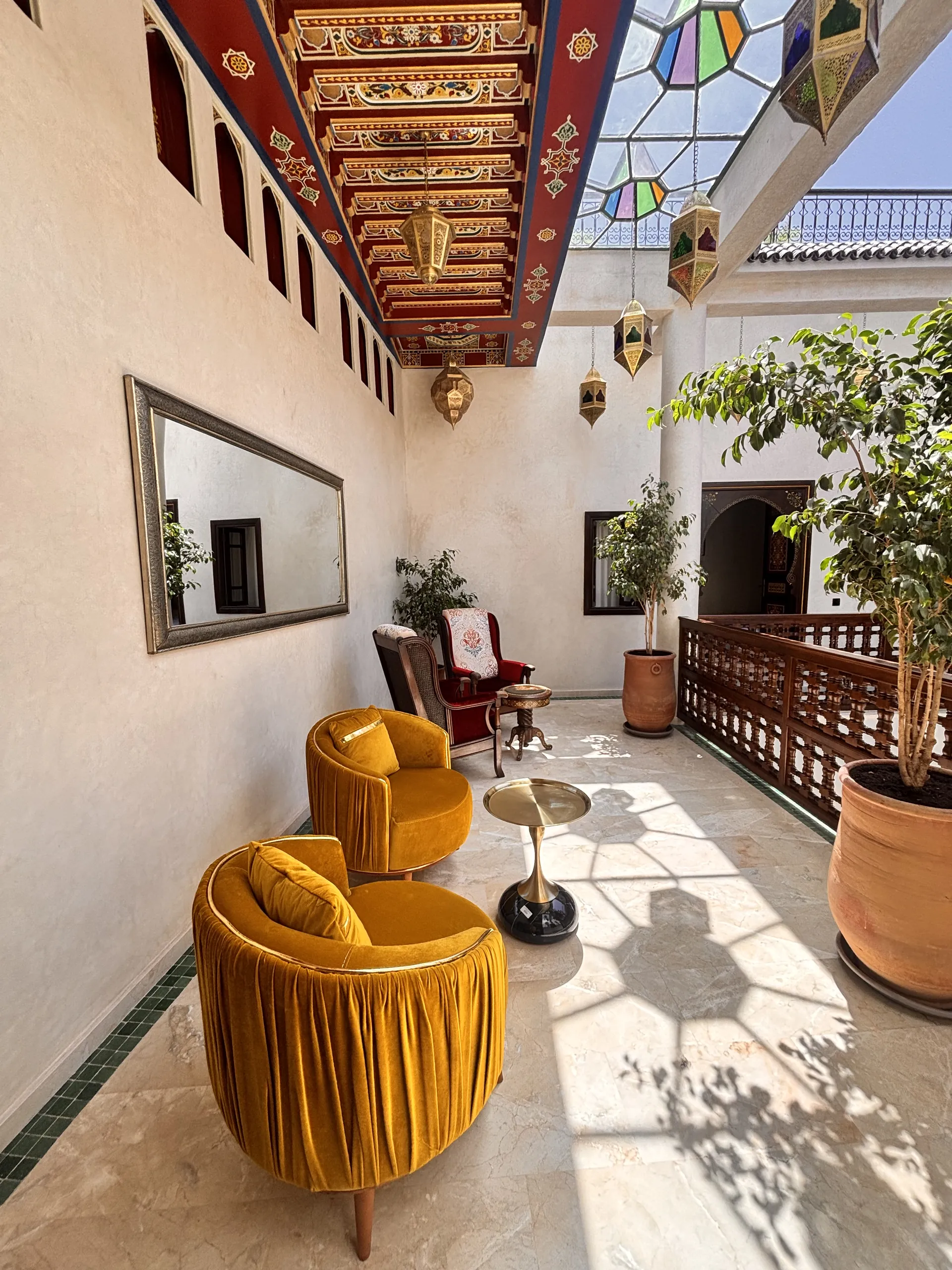 The gallery salon: ochre armchairs, mirror and plants under the painted ceiling